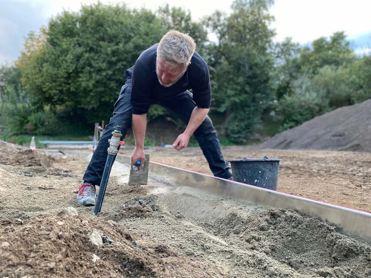 Person richtet mit Werkzeug eine Sandfläche auf einer Baustelle her
